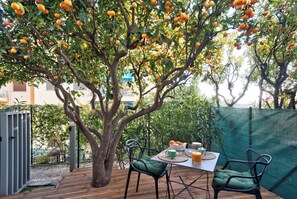 An outdoor seating area with a table and chairs, surrounded by a tree with ripe oranges.