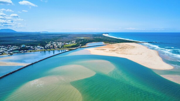 Vista aérea de una zona costera con playa, muelle y pueblo.