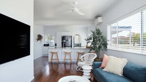 Un salón moderno con un sofá azul, una mesa de centro blanca y un televisor blanco montado en la pared.