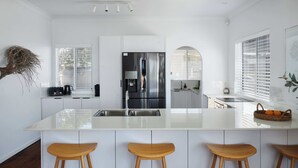 Una cocina moderna con armarios blancos, electrodomésticos de acero inoxidable, una isla central con taburetes y una planta colgante.