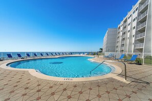 Una piscina con un indicador de profundidad de 3 pies, rodeada de sillas de descanso y un edificio con balcones.