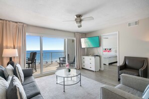 Habitación de hotel con balcón, cama, televisor, escritorio y sofá.