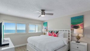 A bedroom with a bed, white nightstands, a ceiling fan, and artwork on the walls.