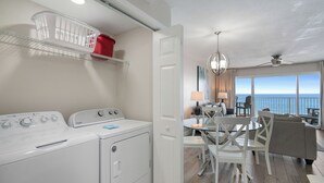 A laundry area with a washer and dryer, a dining area with a table and chairs, and a view of the ocean through large windows.