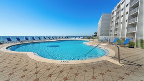 A swimming pool with a 3 FT depth marker, surrounded by lounge chairs and a building with balconies.