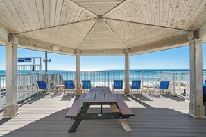 Una terraza de madera con una mesa de picnic y sillas azules, con vista a la playa.