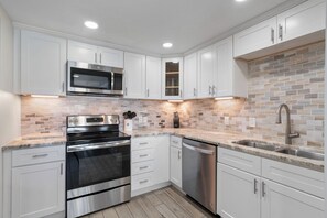 A modern kitchen with white cabinets, stainless steel appliances, and a tiled backsplash.