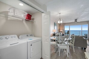 A laundry area with a washer and dryer, a dining area with a table and chairs, and a view of the ocean through large windows.