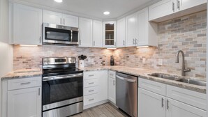 A modern kitchen with white cabinets, stainless steel appliances, and a tiled backsplash.