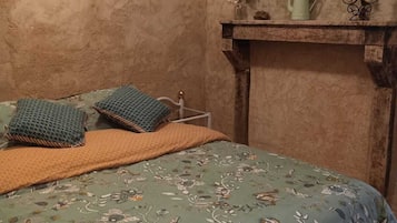 Cozy bedroom with a floral-patterned bedspread, woven throw blanket, and a shelf with decorative accents.