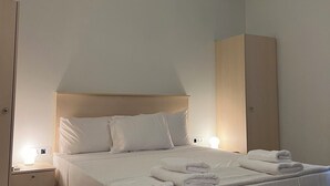 Een opgemaakt bed met witte lakens, een bedlamp en een hanglamp in een minimalistisch ingerichte kamer.