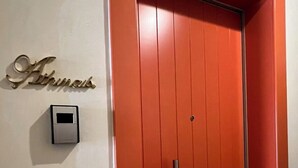 Een rode deur met een handgreep en een klein intercomsysteem aan de zijkant.