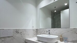 Een moderne badkamer met een witte wastafel, een marmeren aanrechtblad en een grote spiegel.