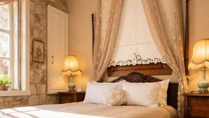 Une chambre à coucher avec un lit à baldaquin, un mur en pierre, une fenêtre donnant sur un beau paysage et une table de chevet avec une lampe.