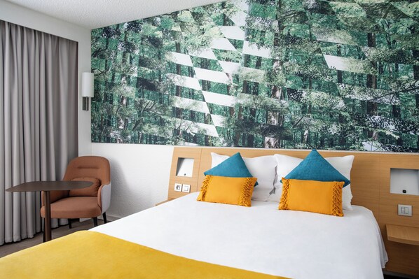Una habitación de hotel con cama, una silla, una mesa y un gran mural en la pared.