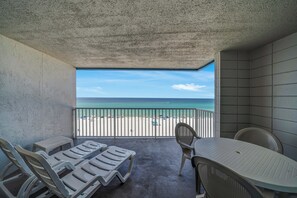 Ein Balkon mit Blick auf den Strand, Liegestühlen und einem Tisch.