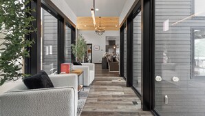 Ein modernes Interieur mit einer Diele, die zu einer Küche führt, mit Holzboden, großen Fenstern und einer Tür mit schwarzem Rahmen.