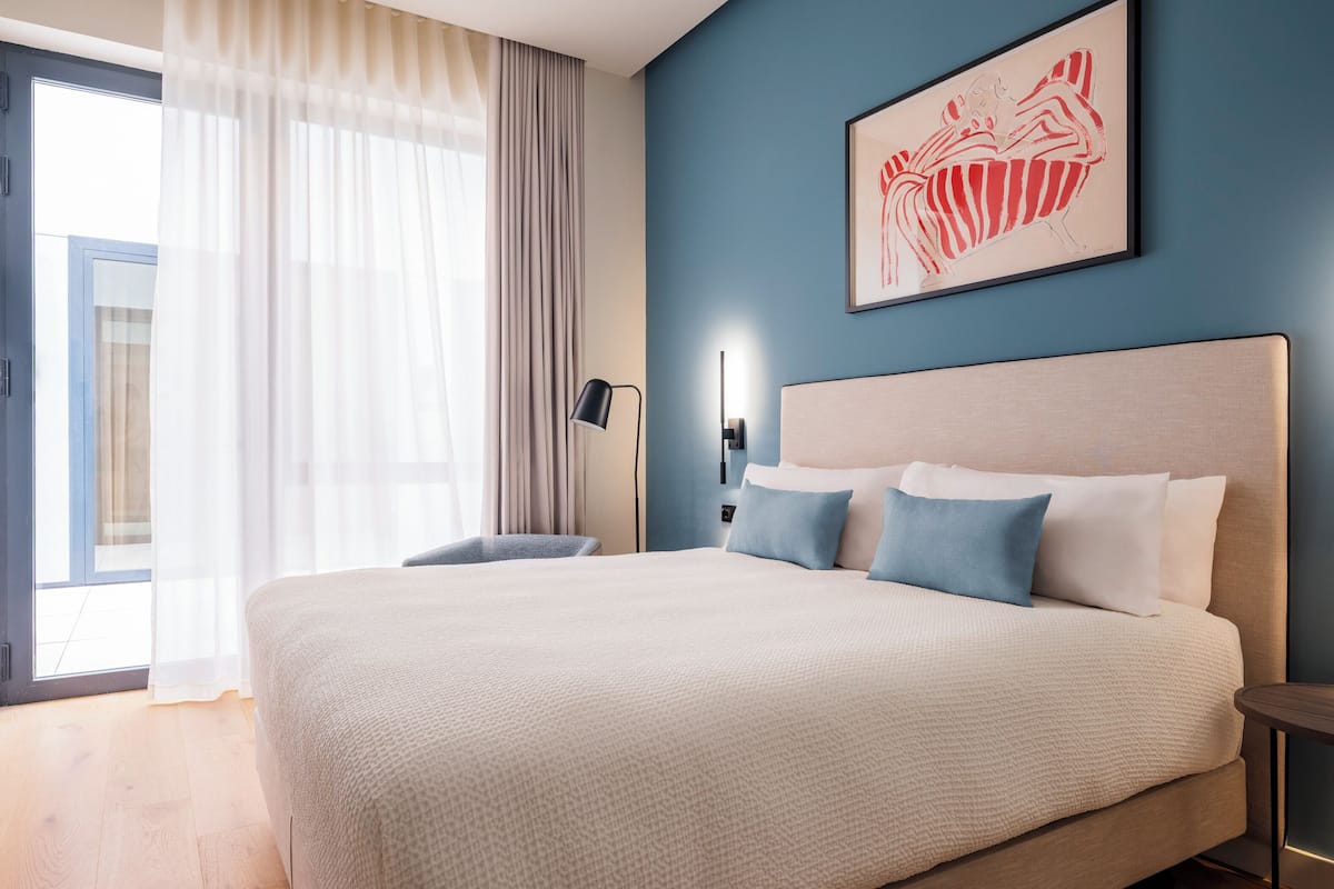 A modern hotel room with a large bed, a desk, and a view of the outdoors.