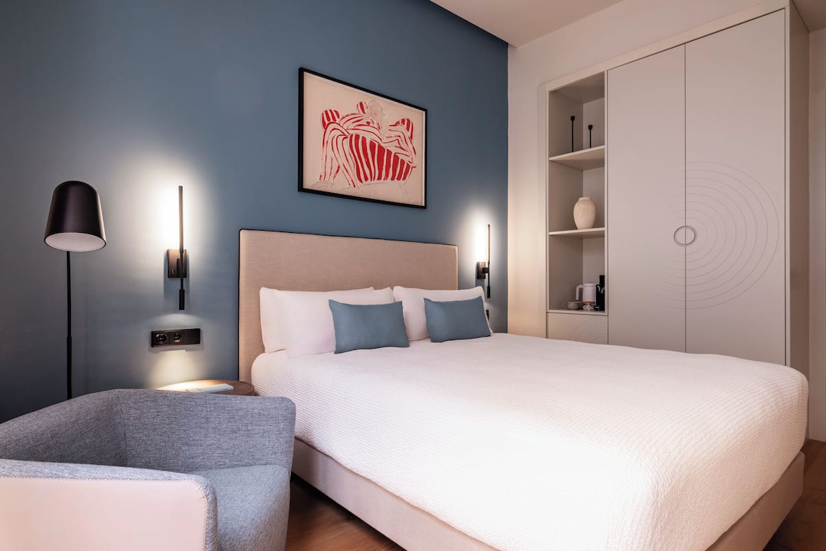 A modern bedroom with a large bed, bedside tables, a floor lamp, a wall-mounted artwork, and a wardrobe.