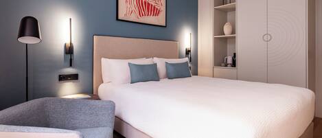 A modern bedroom with a large bed, bedside tables, a floor lamp, a wall-mounted artwork, and a wardrobe.