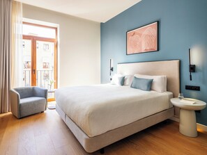 A modern hotel room with a large bed, a bedside table, a chair, and a view of the outside. - Numa Valencia La Xerea (Valencia)
