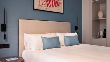 A neatly made bed with a beige headboard, white and blue pillows, and a framed artwork above it.