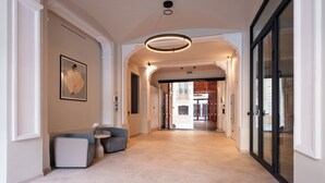 Un pasillo amplio con techo alto, una lámpara moderna y un área de descanso con una mesita y sillas.