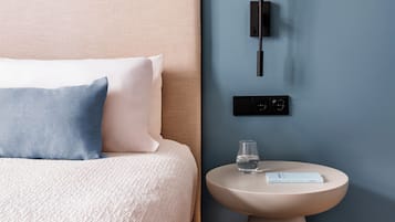 A neatly arranged bedroom with a bed, pillows, a bedside table with a glass of water, and a wall-mounted light fixture.