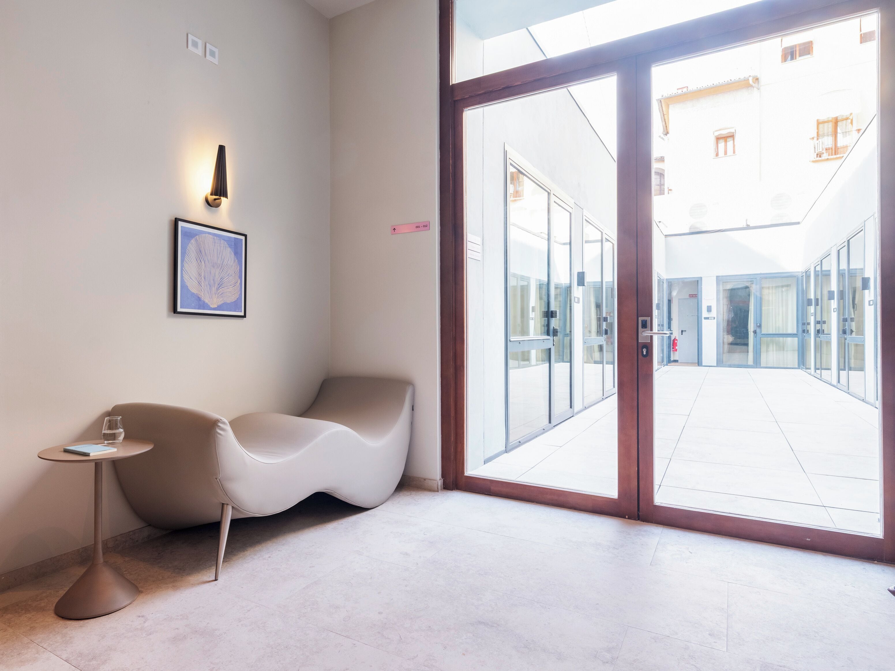 A modern interior with a curved seating area, a small table with a glass, and a large glass door leading to an outdoor space.