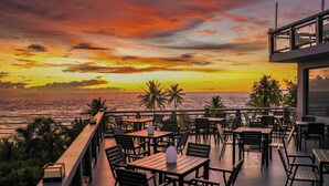 Une terrasse avec des tables et des chaises donnant sur un coucher de soleil sur l’océan.