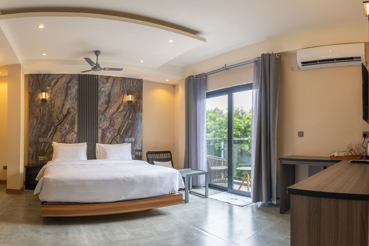 A modern bedroom with a curved bed, a ceiling fan, and a balcony with a view of greenery.