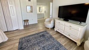 A living room with a flat-screen TV, a white dresser, a patterned rug, and a small stool. - 1703 Brighton, newly remodeled condo with full access! (Myrtle Beach)