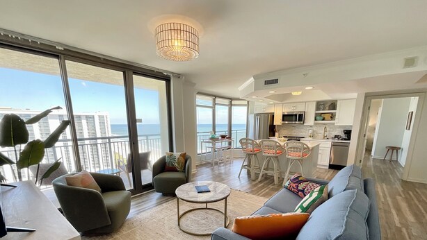 A spacious living area with a large sofa, a coffee table, and a balcony with a view of the ocean. - 1703 Brighton, newly remodeled condo with full access! (Myrtle Beach)