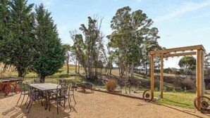 An outdoor seating area with a table and chairs, surrounded by trees and a wooden pergola. - Cooinda, A 3 bedroom home near Mayfield Gardens (Oberon)