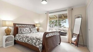 A bedroom with a bed, bedside tables, a mirror, and a window with a view. - Cooinda, A 3 bedroom home near Mayfield Gardens (Oberon)