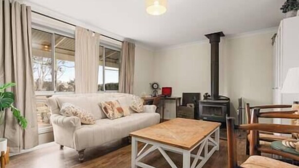 A cozy living room with a sofa, a wooden coffee table, a fireplace, and a dining area with chairs. - Cooinda, A 3 bedroom home near Mayfield Gardens (Oberon)
