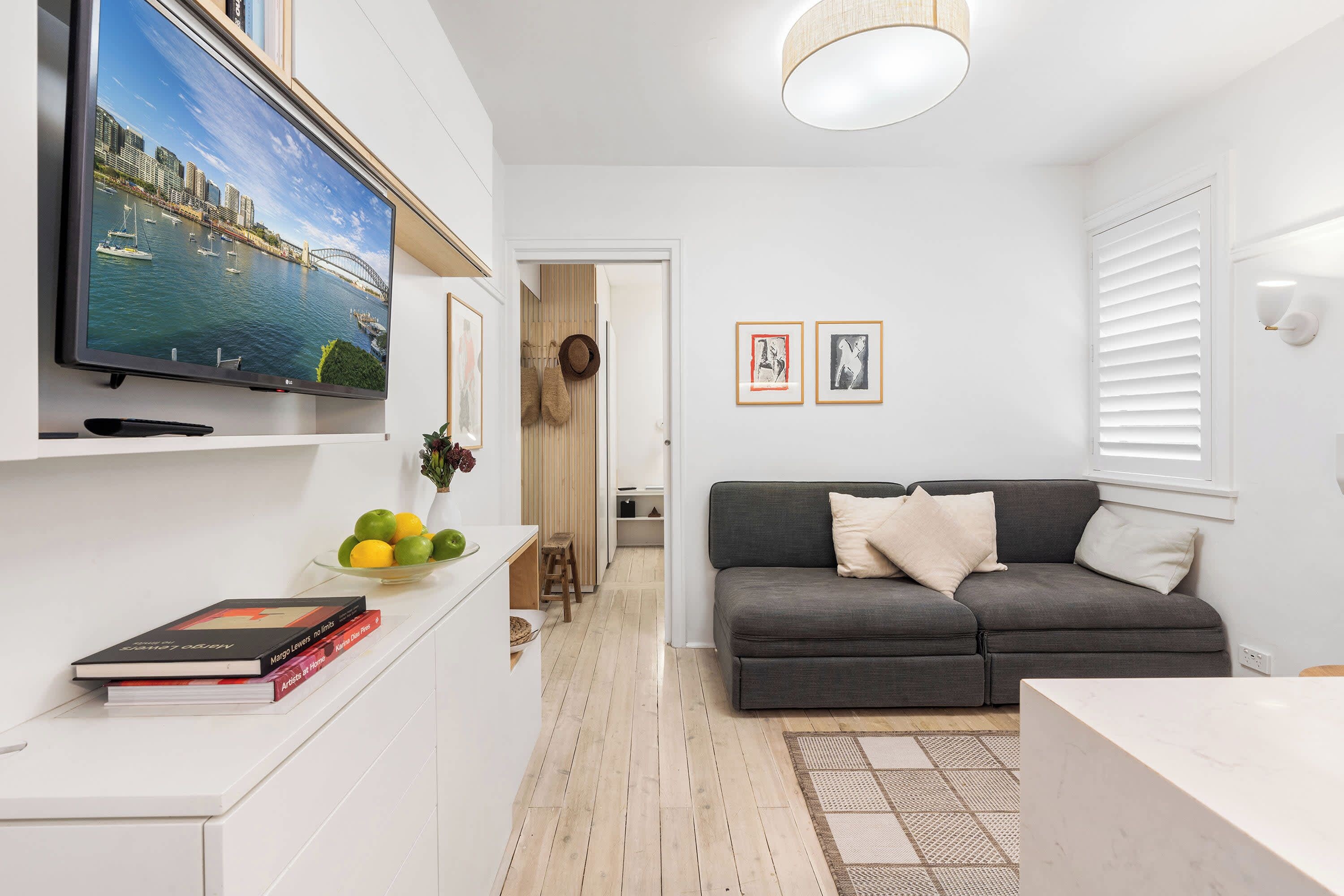 A modern living room with a flat-screen TV, a grey sofa, and a dining area with a white table.