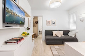 A modern living room with a flat-screen TV, a grey sofa, and a dining area with a white table.