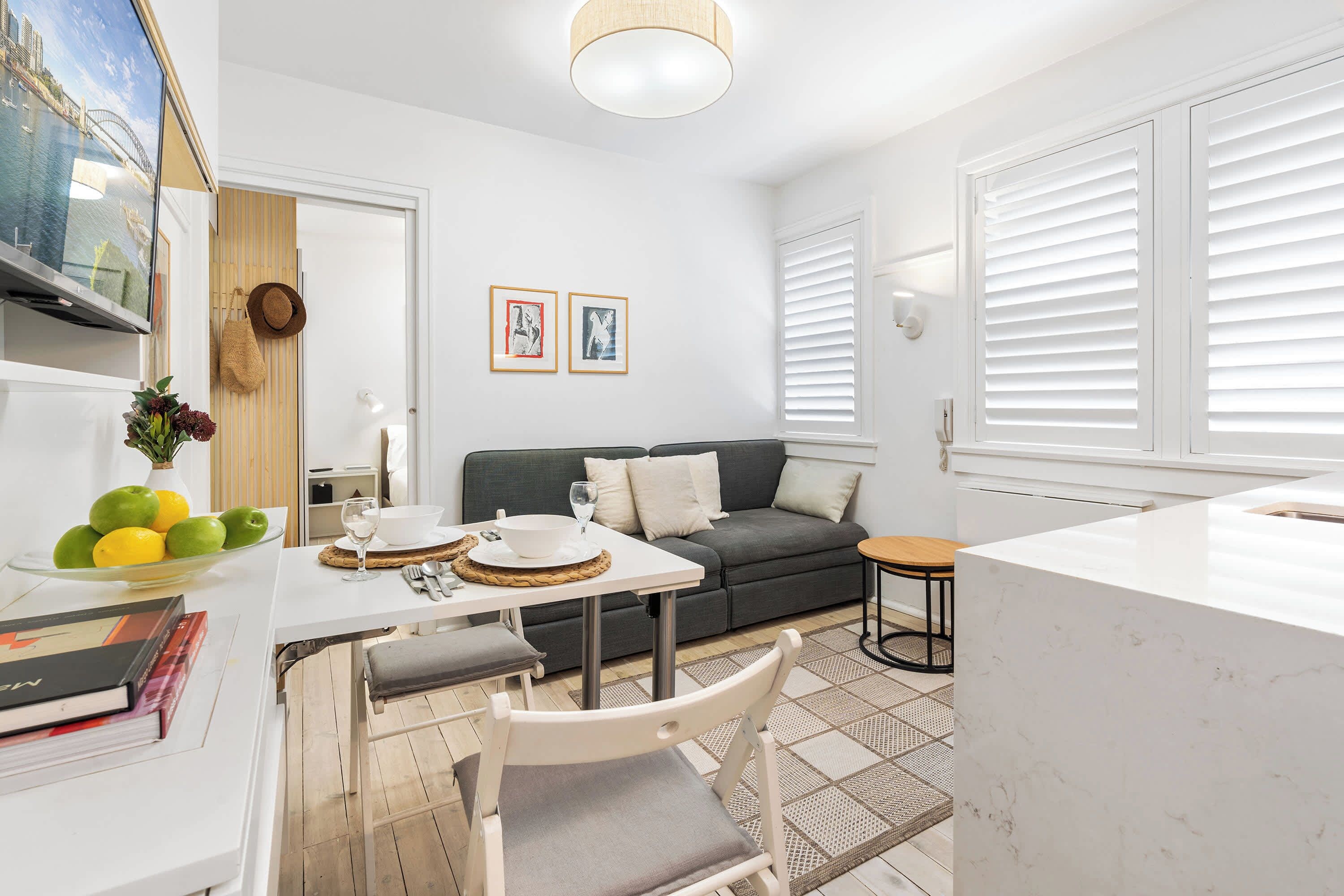 Un salon moderne comprenant un canapé, une table à manger avec des chaises, un téléviseur fixé au mur et un coin cuisine avec un plan de travail.