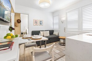 A modern living room with a sofa, a dining table with chairs, a TV mounted on the wall, and a kitchen area with a countertop. - Bay View in Rushcutters Bay (Rushcutters Bay)