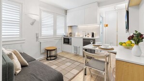 A compact kitchen with white cabinets, a dining table with chairs, and a small stool. - Bay View in Rushcutters Bay (Rushcutters Bay)