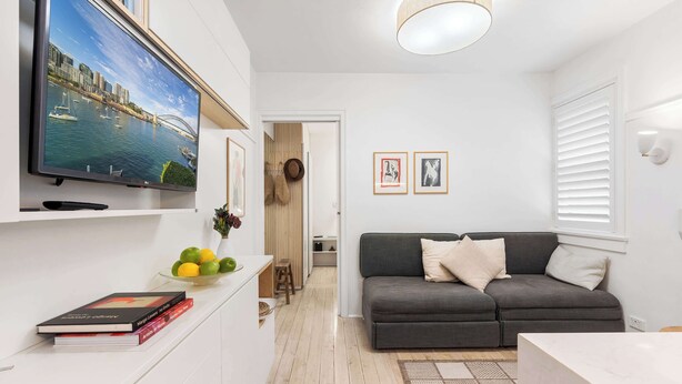 A modern living room with a flat-screen TV, a grey sofa, and a dining area with a white table. - Bay View in Rushcutters Bay (Rushcutters Bay)