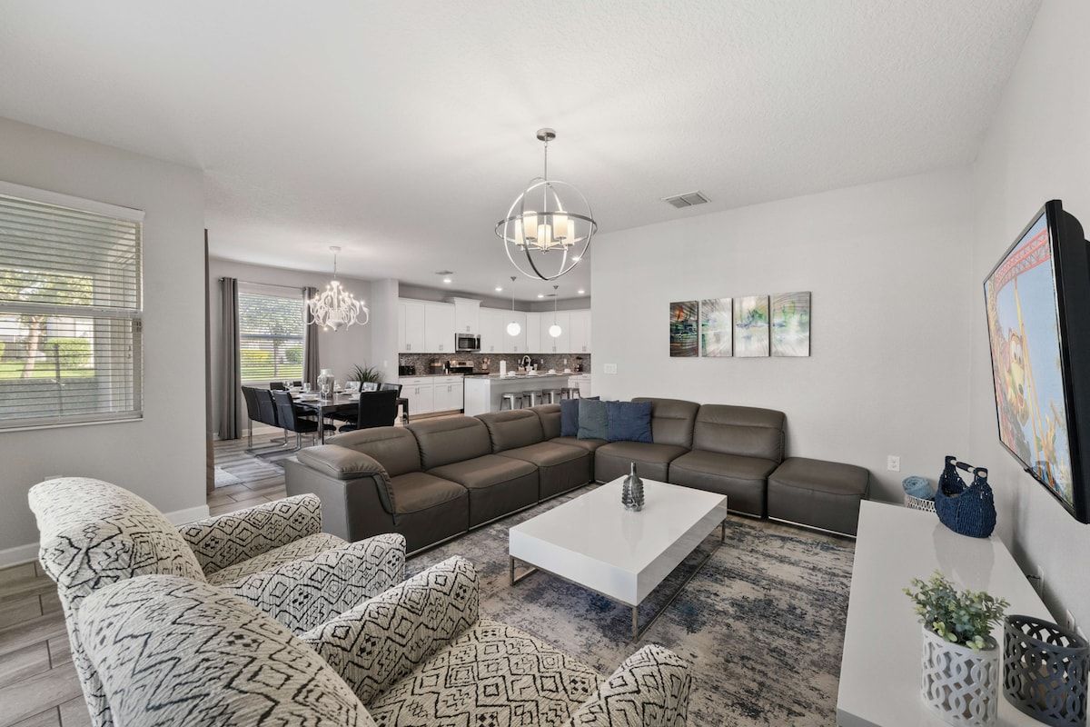 A modern living room with a sectional sofa, a coffee table, and a dining area in the background.