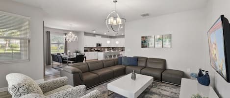 Uma sala de estar moderna com um sofá seccional, uma mesa de centro e uma área de jantar ao fundo.