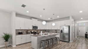 A modern kitchen with white cabinets, a granite countertop, stainless steel appliances, and a central island with bar stools. - Disney Escape: Private Pool and Spa, Near Disney World ! (Kissimmee)