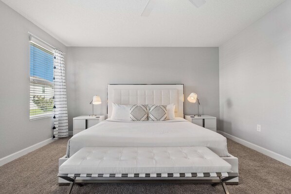 Une chambre à coucher avec un grand lit, deux tables de chevet et une fenêtre avec des stores.