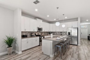 A modern kitchen with white cabinets, a central island with stools, stainless steel appliances, and a potted plant.