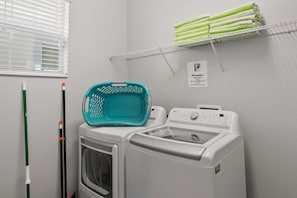 A laundry area with a washing machine, a dryer, a green laundry basket, and a rack with folded towels.