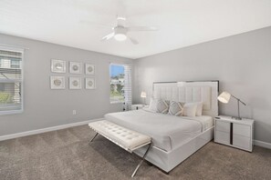 A bedroom with a bed, bedside tables, a bench, a ceiling fan, and framed pictures on the wall.