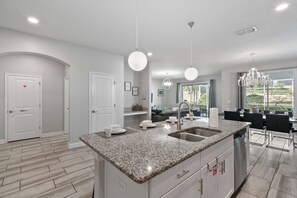 A modern kitchen with a granite countertop, stainless steel sink, and pendant lighting. - Resort Access: 6BR Home w Pool near Disney (Kissimmee)